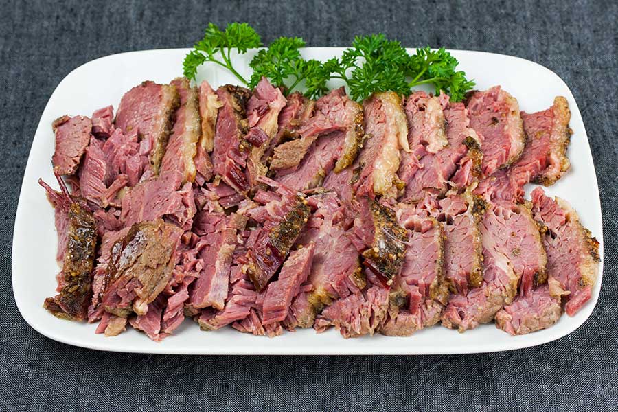 Sliced corned beef on a white platter garnish with fresh parsley.