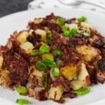 Corned Beef Hash on a white plate garnished with diced green onions.