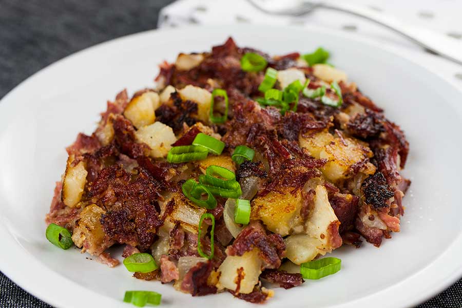 Corned Beef Hash on a white plate garnished with diced green onions.