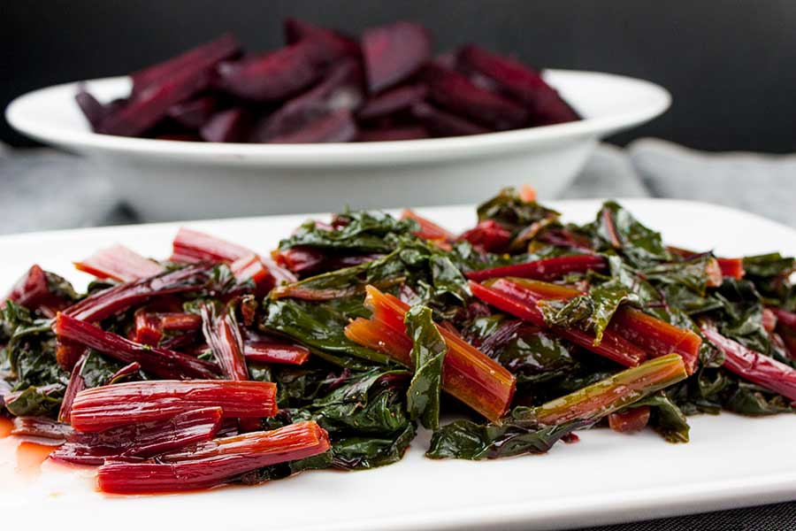 Ninja Foodi fresh beet greens on a white platter with fresh beets in the background.