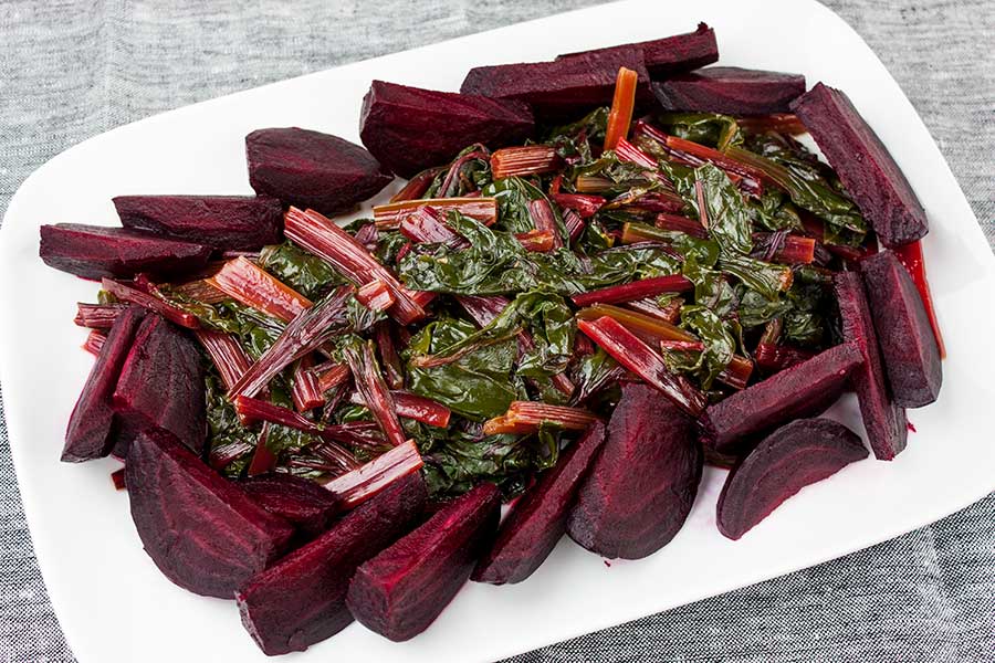 cooked beet greens on a white platter surrounded by cooked beets