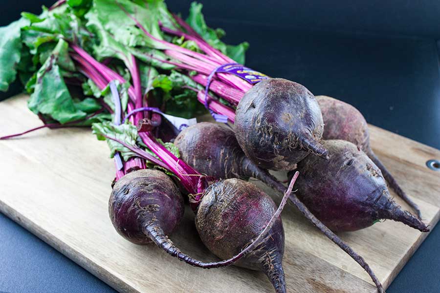 Fresh beets with greens attached on a wooden cutting board.