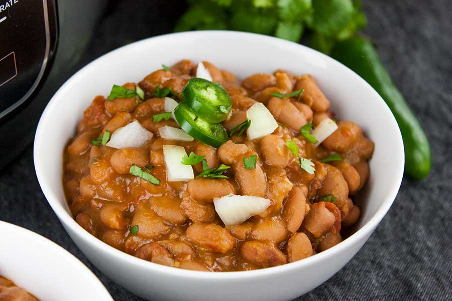 Ninja Foodi Mexican pinto beans (charro beans) in a white bowl with a jalapeno and onion garnish.