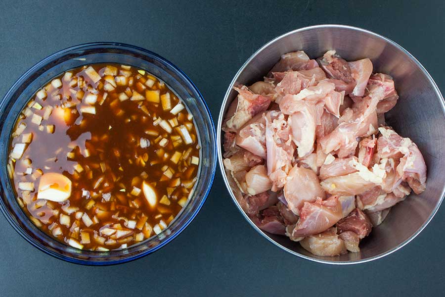 Filipino Chicken Kebabs - Tired of your standard grilled chicken? You have to try these deliciously flavorful Filipino chicken kebabs. Quick and easy and bursting with Asian flavors. cubed chicken in a metal bowl next to marinade in a blue glass bowl