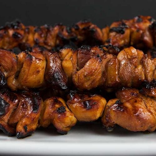 Filipino chicken kebabs on a white plate.