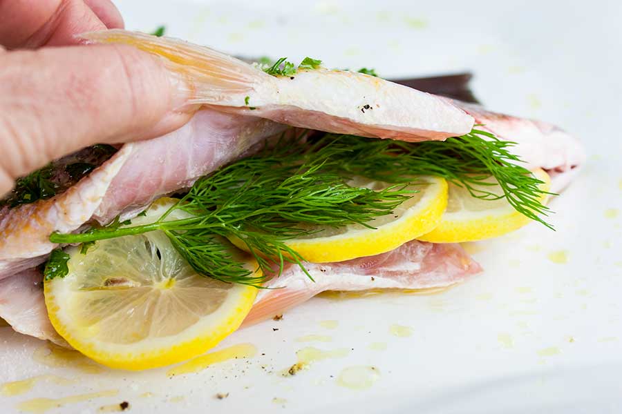 closeup of herbs and lemons slices stuffed into the cavity of a red snapper