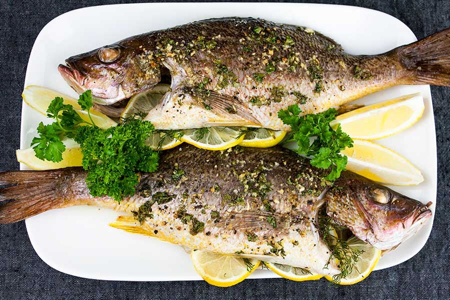 Baked Whole Red Snapper on a white platter garnished with lemon wedges and fresh parsley