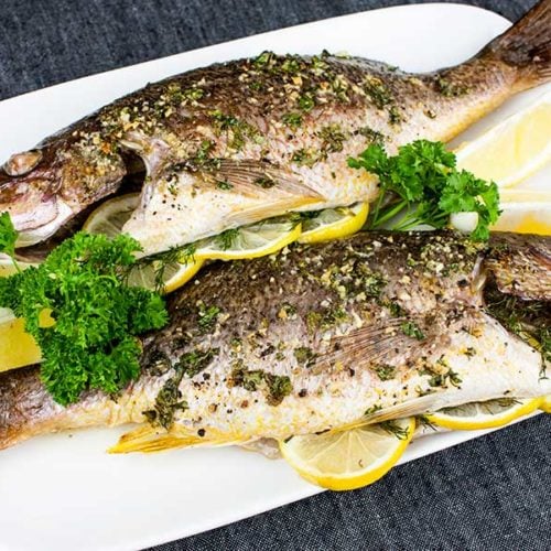 Baked whole red snapper on a white plate garnished with parsley.