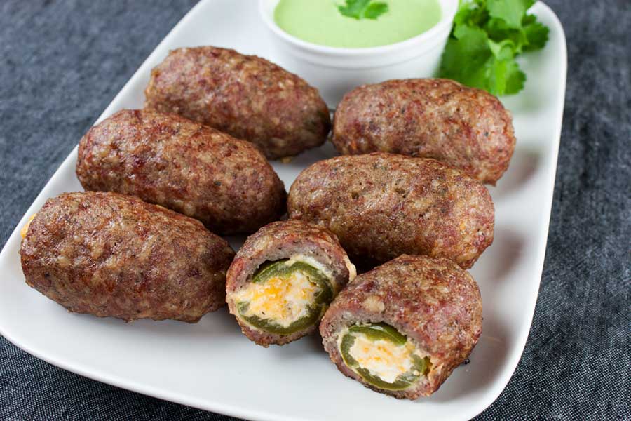 Smoked Keto Armadillo Eggs on a white platter with Jalapeno Cilantro Dip in a white ramekin