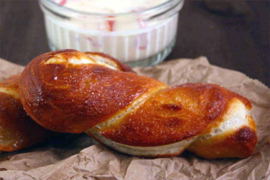 Soft pretzels on brown paper with cheese dip in background.