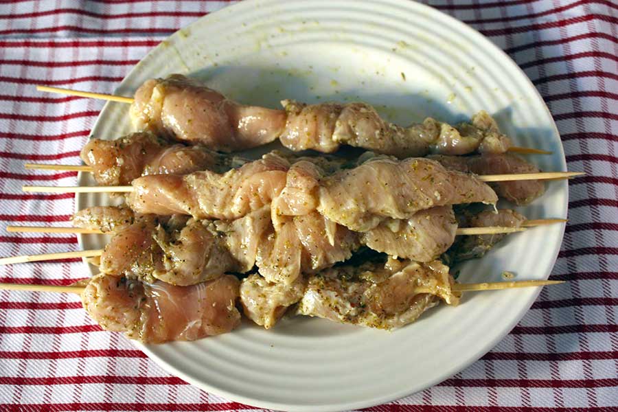 Greek marinated chicken on wooden skewers and stacked on a light plate.