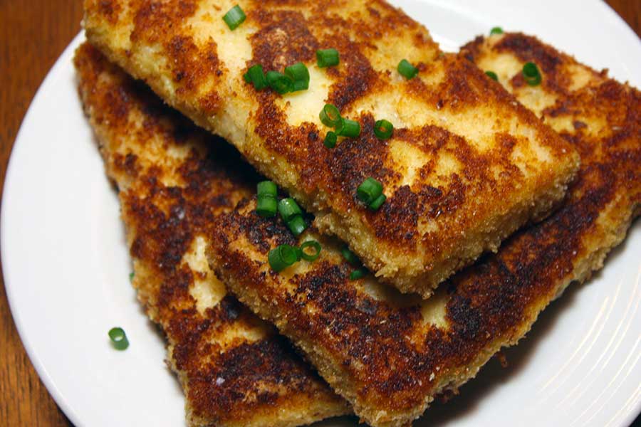 Fried Grit Cakes on a white plate garnished with diced green onions