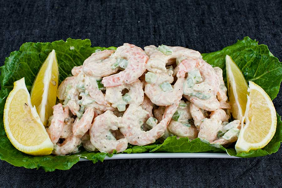 Shrimp salad on a lettuce lined white plate garnished with lemon wedges.
