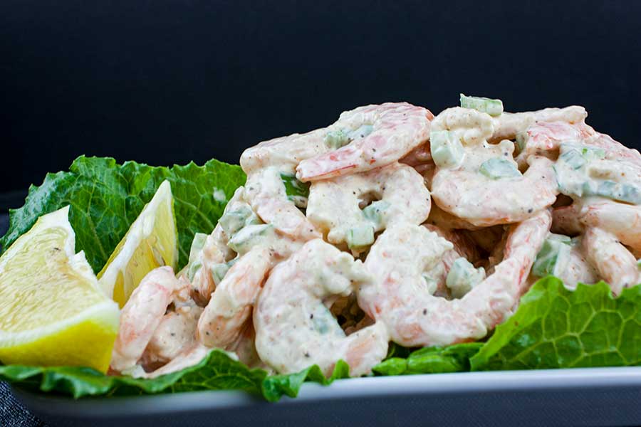 Close up of the shrimp salad on a lettuce lined white plate garnished with lemons.