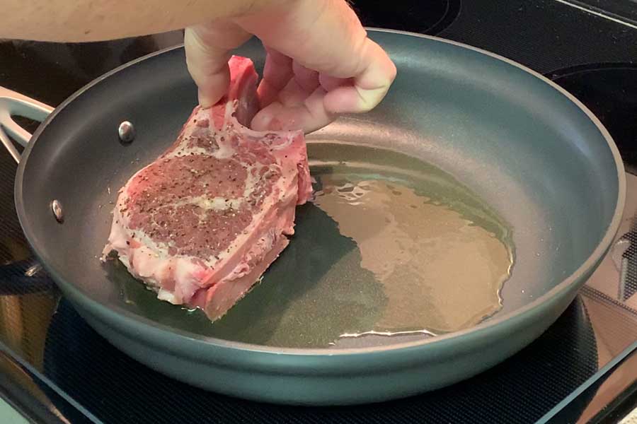 Pork chop being placed in a frying pan