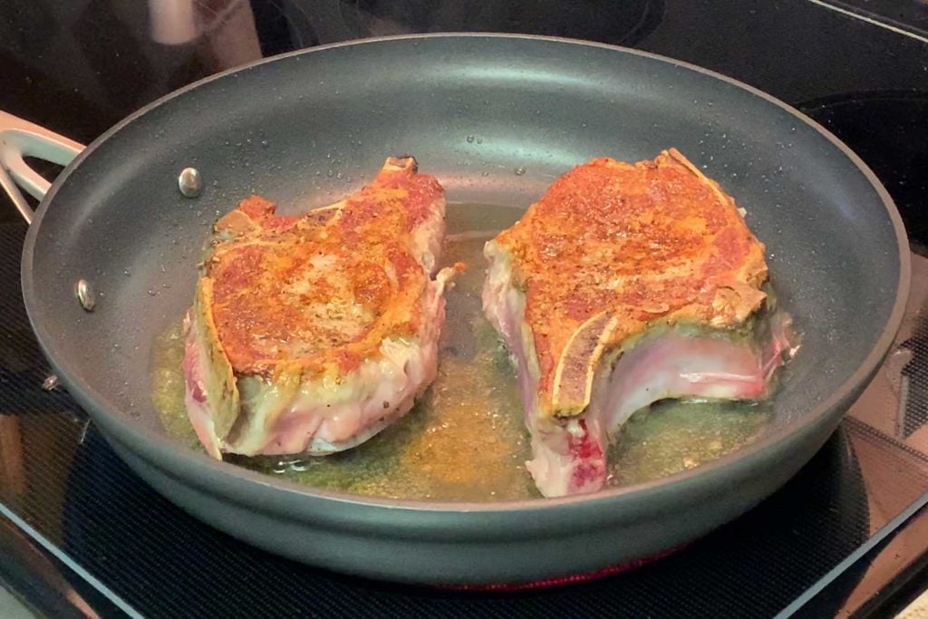 Pork chops cooking in a skillet, one side done