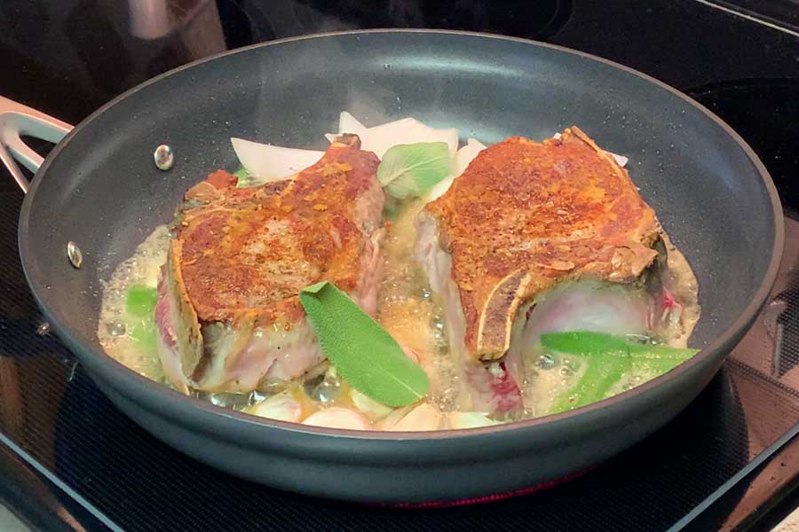 Pork chops with sage cooking in a skillet