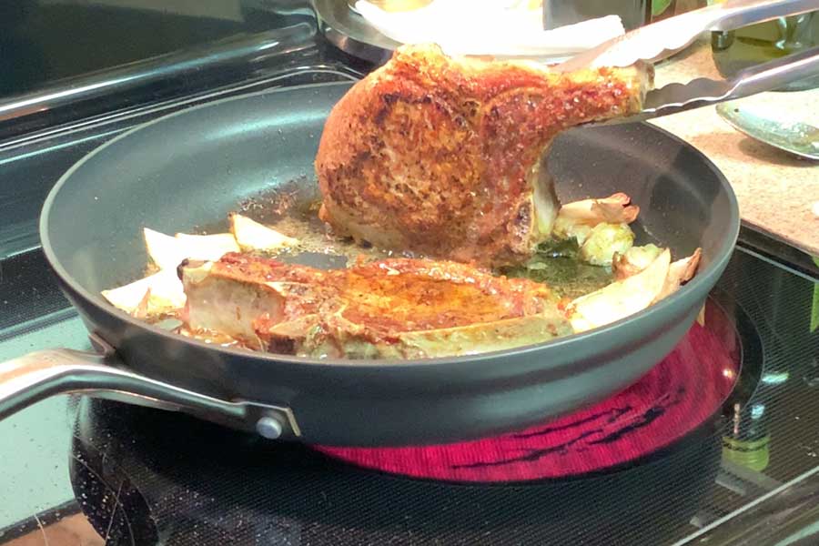 pork chops being seared on the side in a skillet

