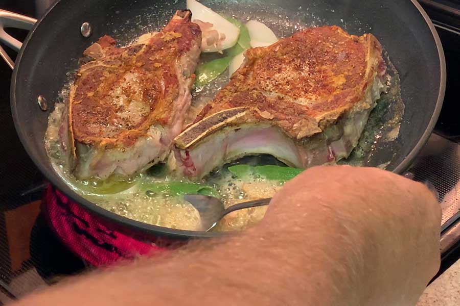 basting pork chops in a skillet with sage and butter