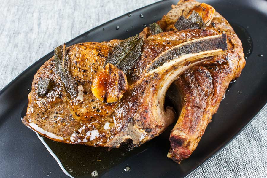 Thick cut bone in pork chops on a black plate.