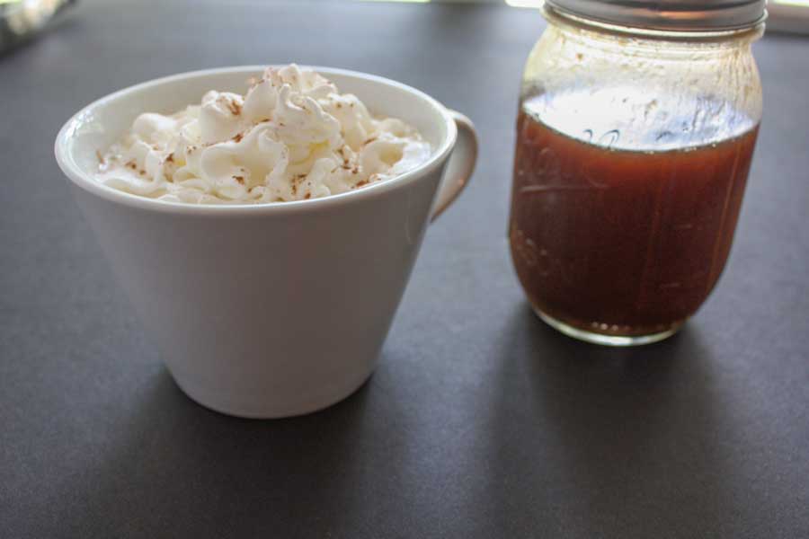 Pumpkin spice latte in a white cup topped with whipped cream and a bottle of the pumpkin syrup sitting next to it.