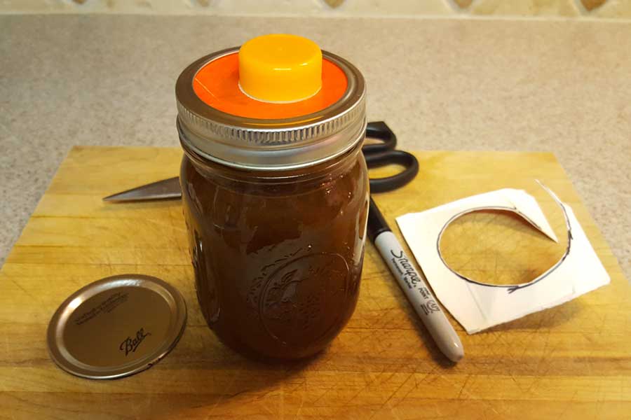 Mason jar filled with pumpkin spice syrup with the orange juice spout inserted under the lid ring.