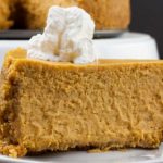 Slice of pumpkin cheesecake garnished with whipped cream on a white plate.