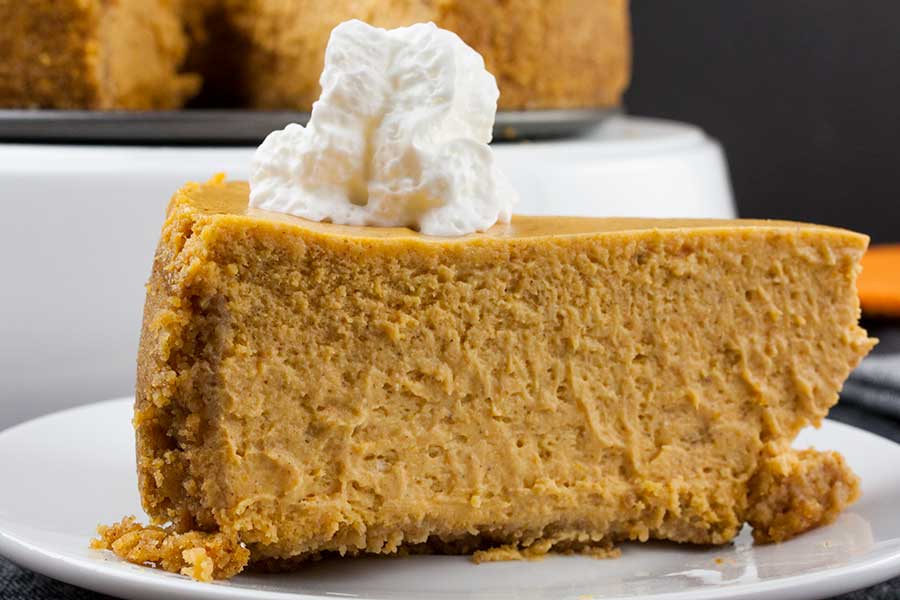 Slice of pumpkin cheesecake topped with whipped cream on a white plate.