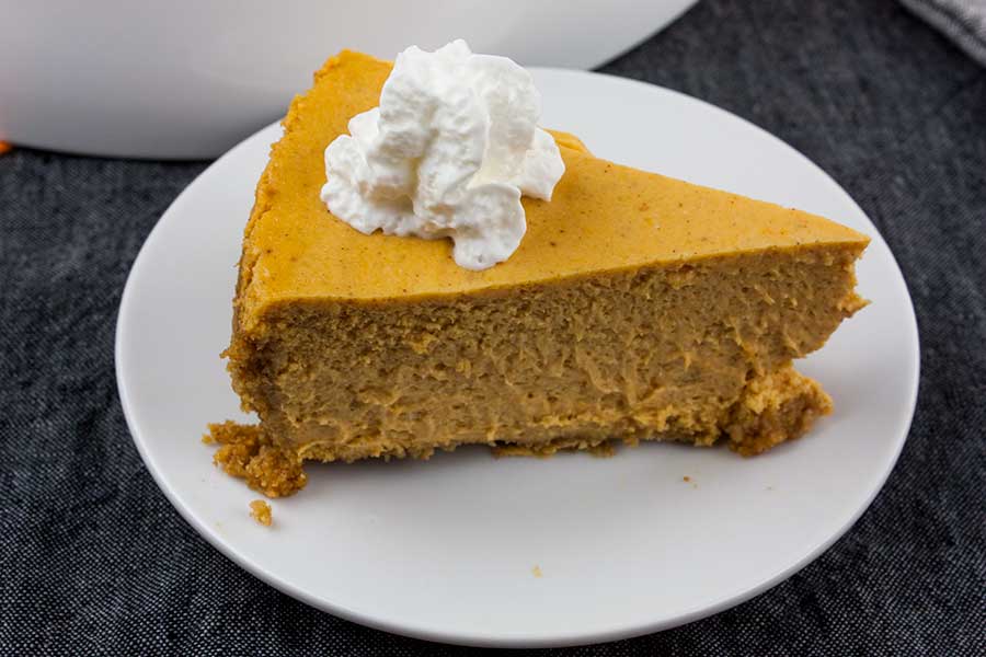 Slice of pumpkin cheesecake topped with whipped cream on a white plate.
