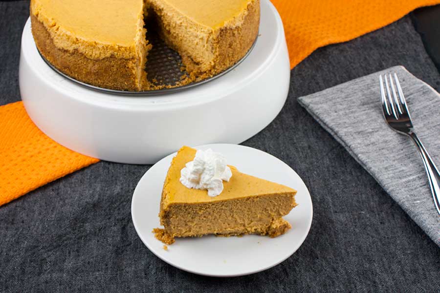 Slice of pumpkin cheesecake topped with whipped cream on a white plate.