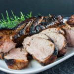 Keto grilled pork tenderloin sliced on a white platter garnished with fresh rosemary.