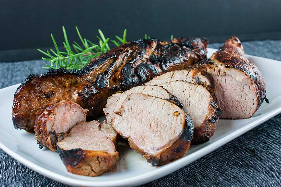 Keto grilled pork tenderloin sliced on a white platter garnished with fresh rosemary.