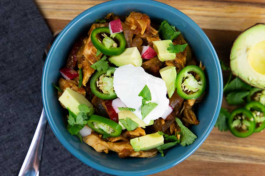 Chicken fajita stew topped with jalapeños, avocado, cilantro and chopped radish in a blue bowl