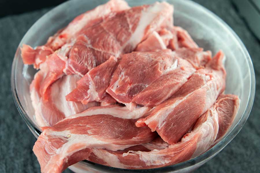 Strips of pork butt in a chilled glass bowl.