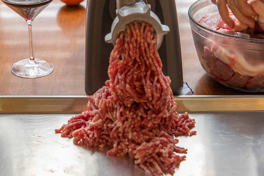 Pork butt being ground in the meat grinder onto a large baking sheet.