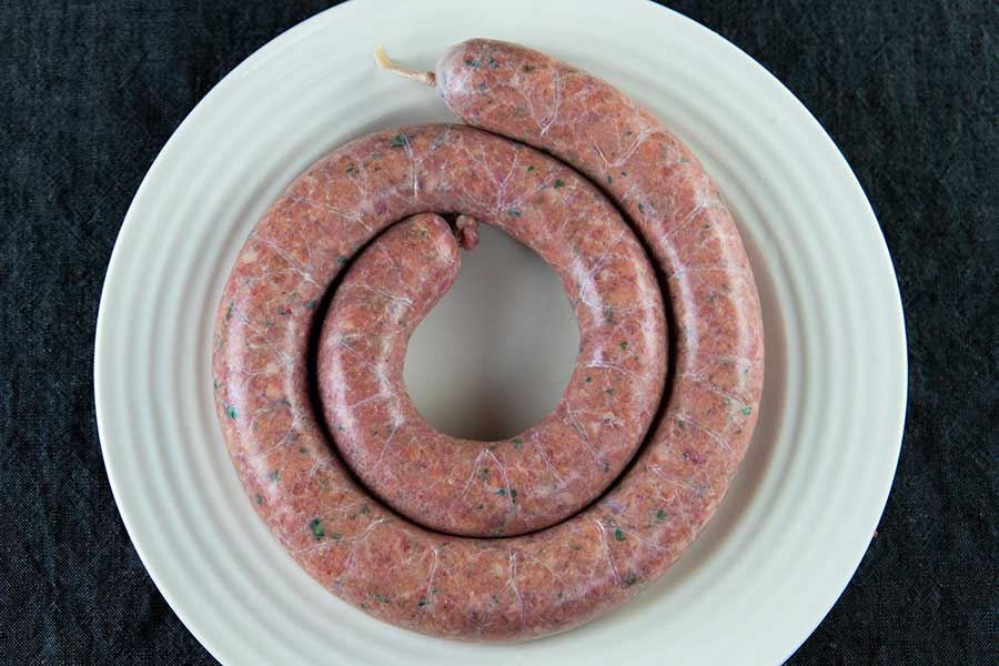 A coil of uncooked Italian sausage on a light plate.