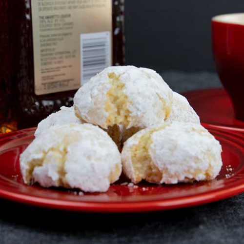 Amaretti cookies stacked on a red plate with a red coffee cup in the background.