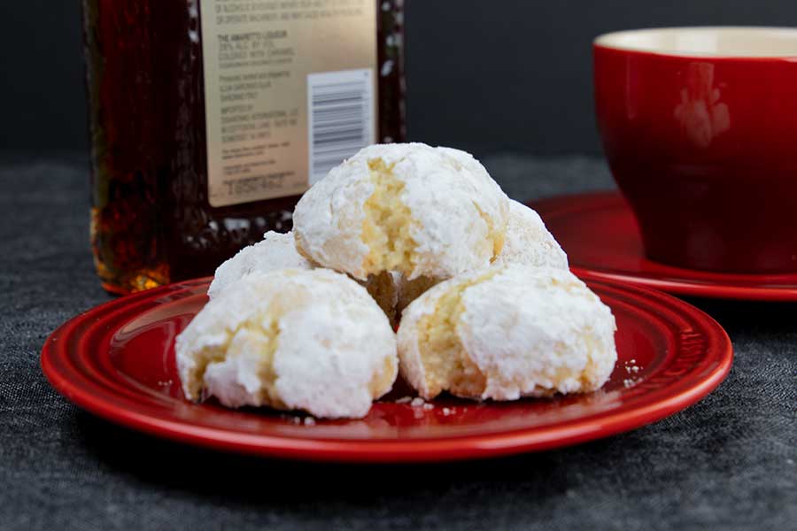 Amaretti cookies stacked on a red plate with a red coffee cup in the background.