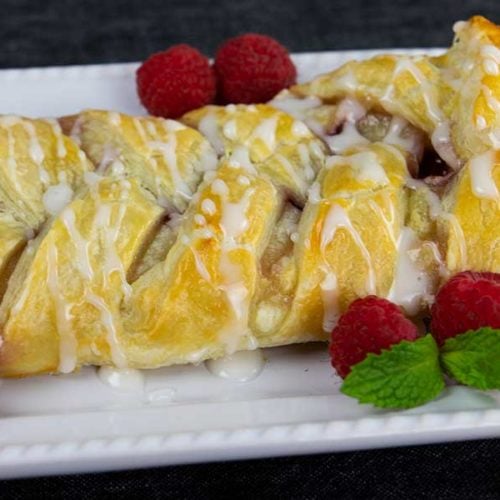 Raspberry cream cheese danish on a white platter garnished with fresh raspberries and mint.