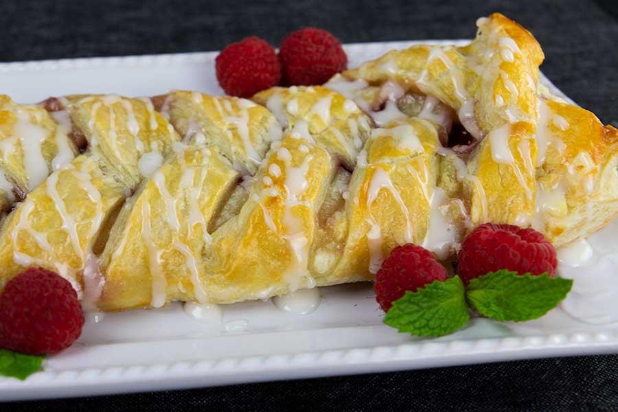 Raspberry cream cheese danish on a white platter garnished with fresh raspberries and mint.
