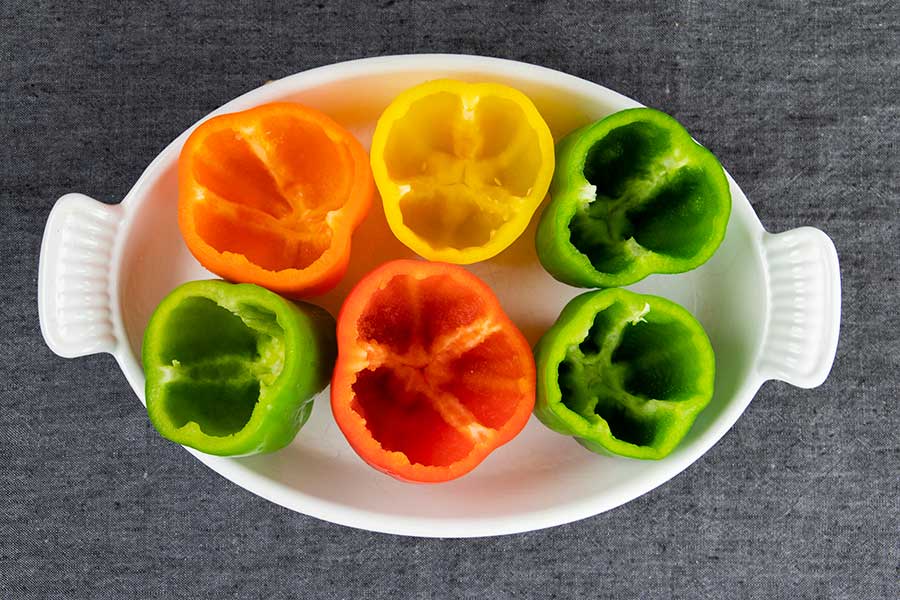 Colored raw bell peppers, tops removed and cored in a white baking dish