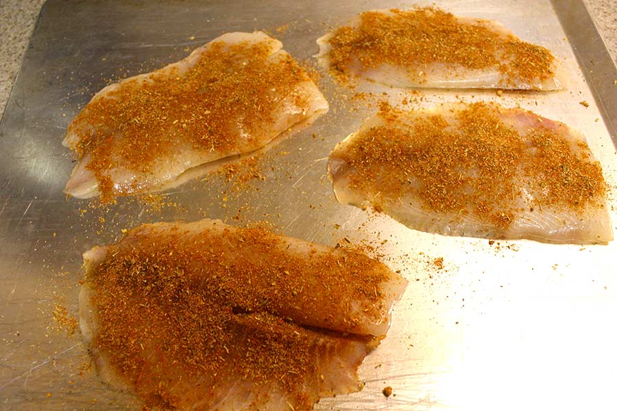 Raw tilapia fish fillets seasoned on a sheet pan.