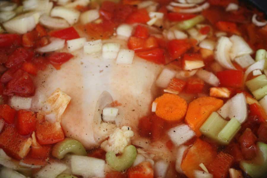 Chicken and vegetables in a pot of water.