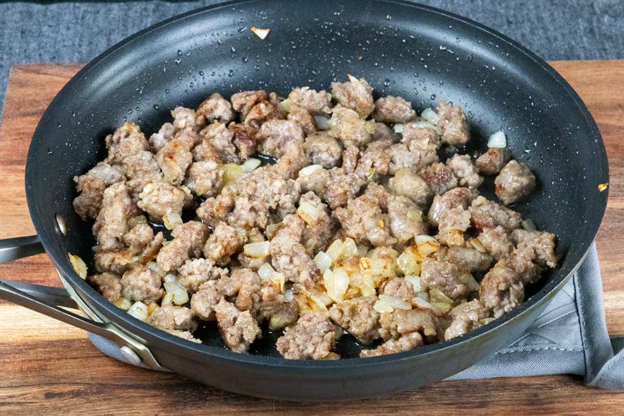 Cooked sausage and chopped onions in a black skillet.