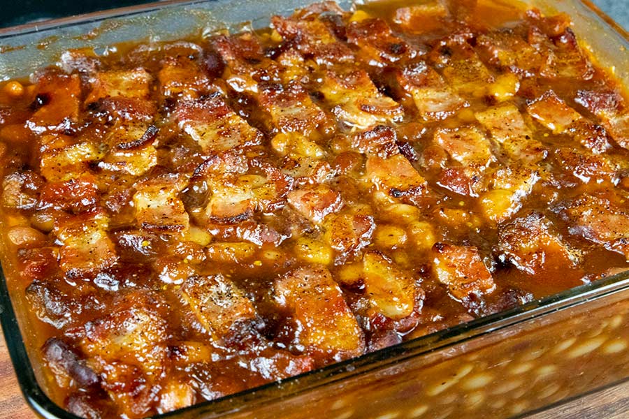 Baked Beans topped with bacon in a glass baking dish.