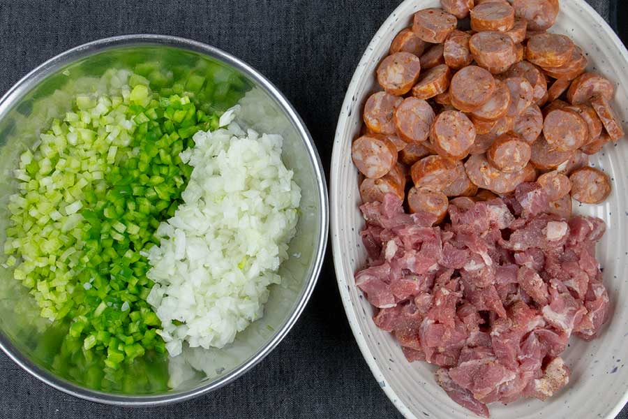 Diced celery, bell pepper, and onions in one bowl, and in another bowl is the diced pork and sausage.