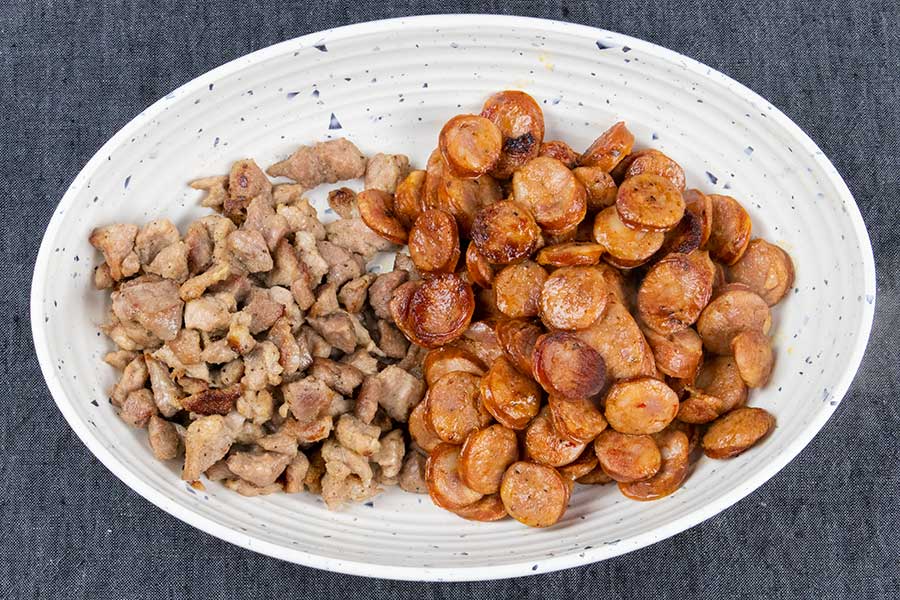 Browned pork and sausage in a white bowl.