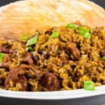 Cajun jambalaya in a white serving bowl with a loaf of bread in the background.