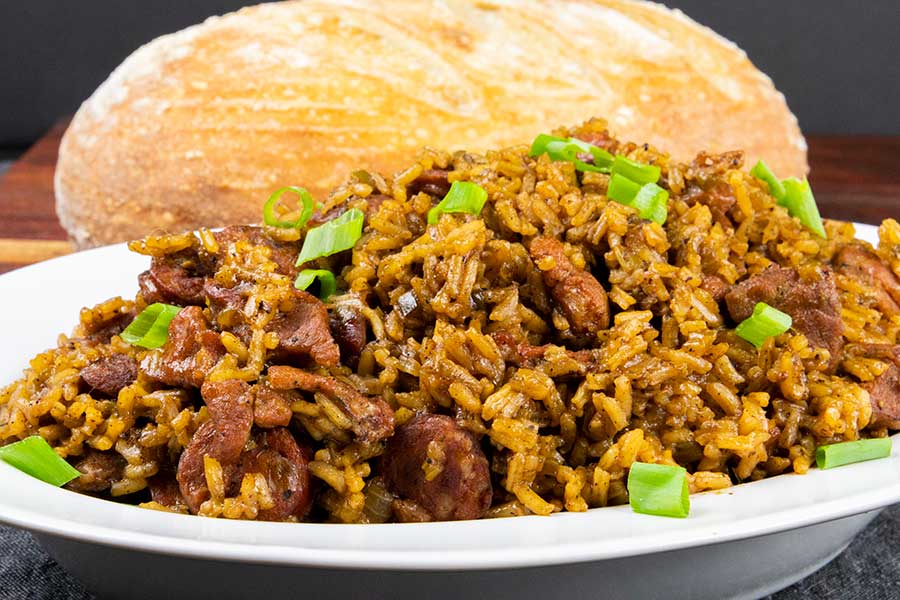 Authentic and amazingly delicious Cajun jambalaya in a white serving bowl with a loaf of bread in the background.