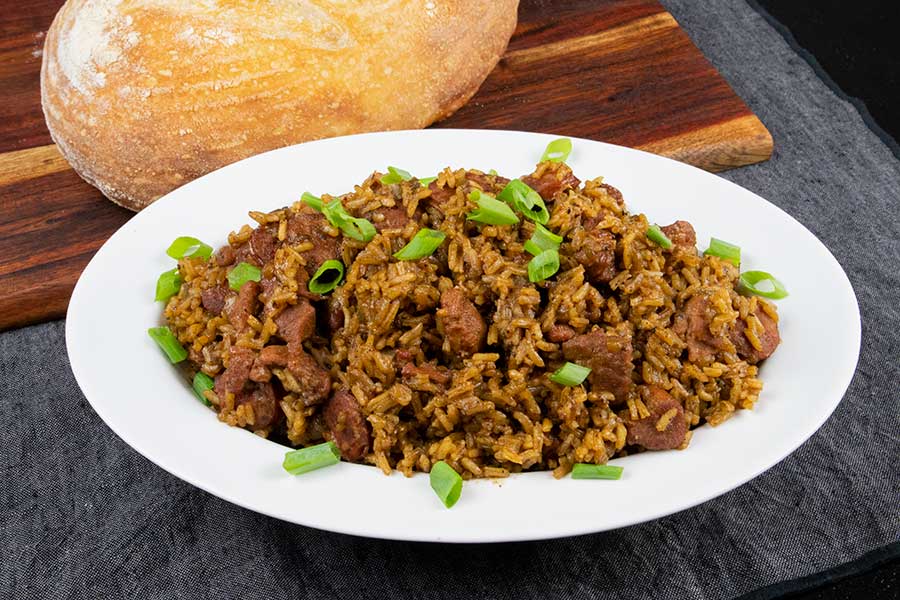 Cajun jambalaya in a white serving bowl with a loaf of sourdough bread in the background.